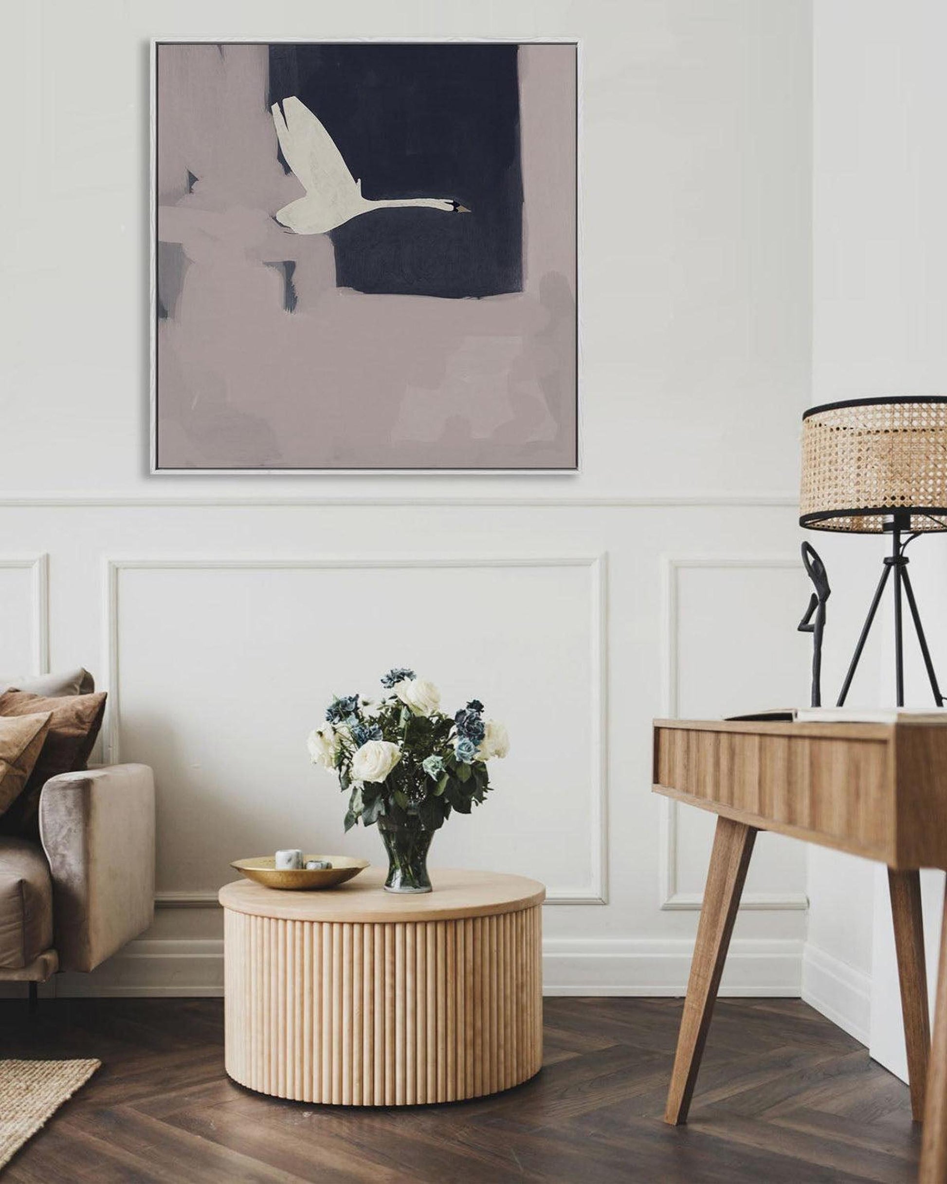 Living room with a painting of a swan, a coffee table with flowers, and a lamp.