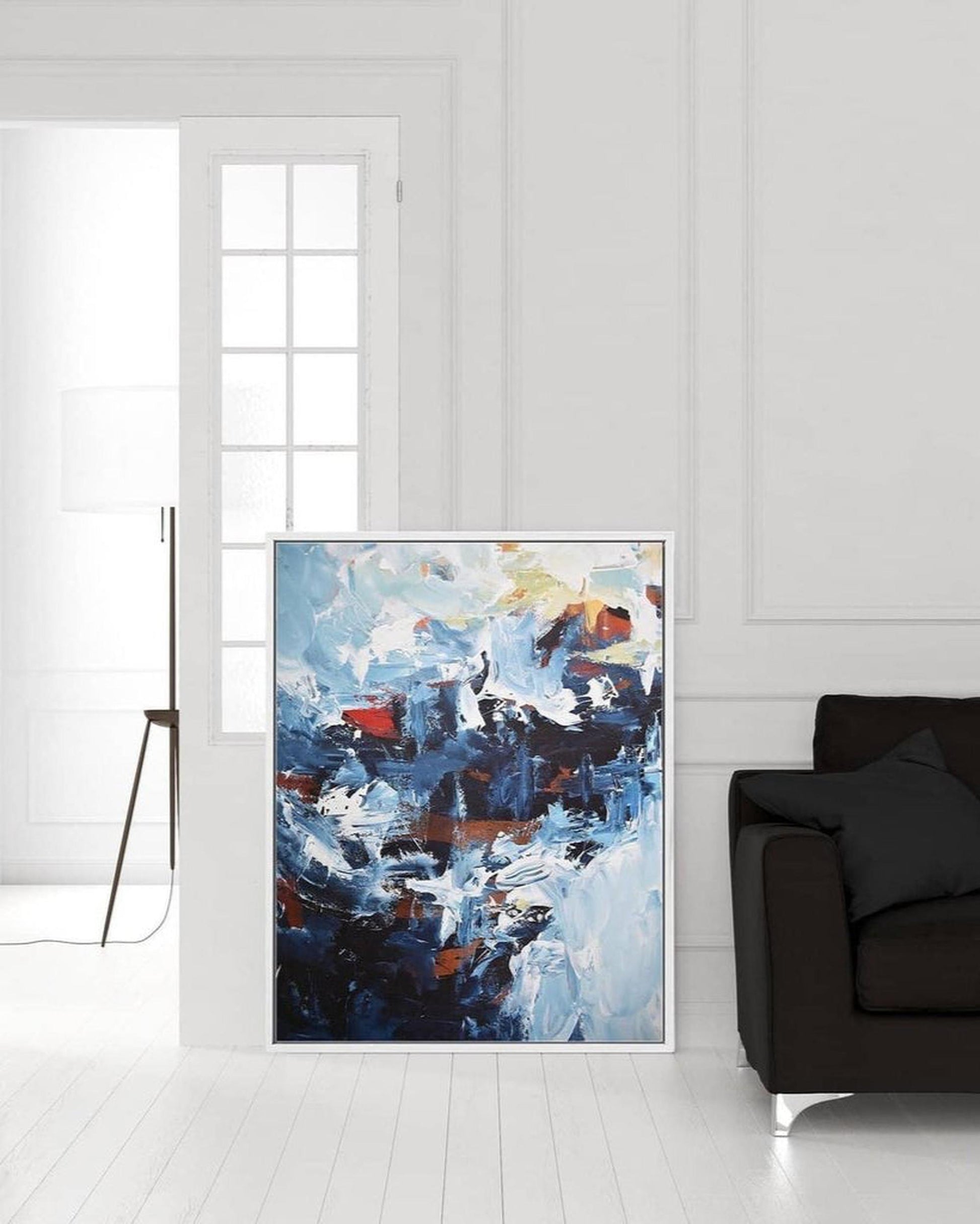 Abstract painting in a modern living room with a white wall and dark sofa.