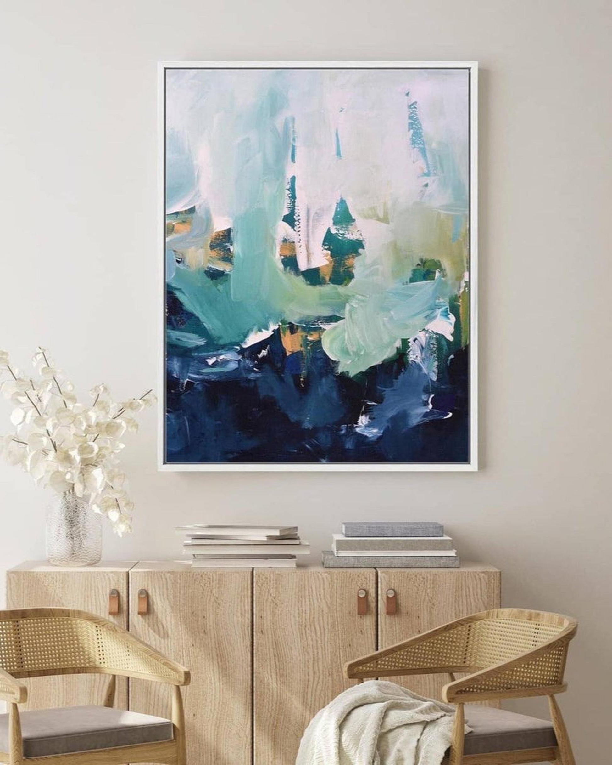 Abstract painting in a modern interior setting with a wooden cabinet and chairs.