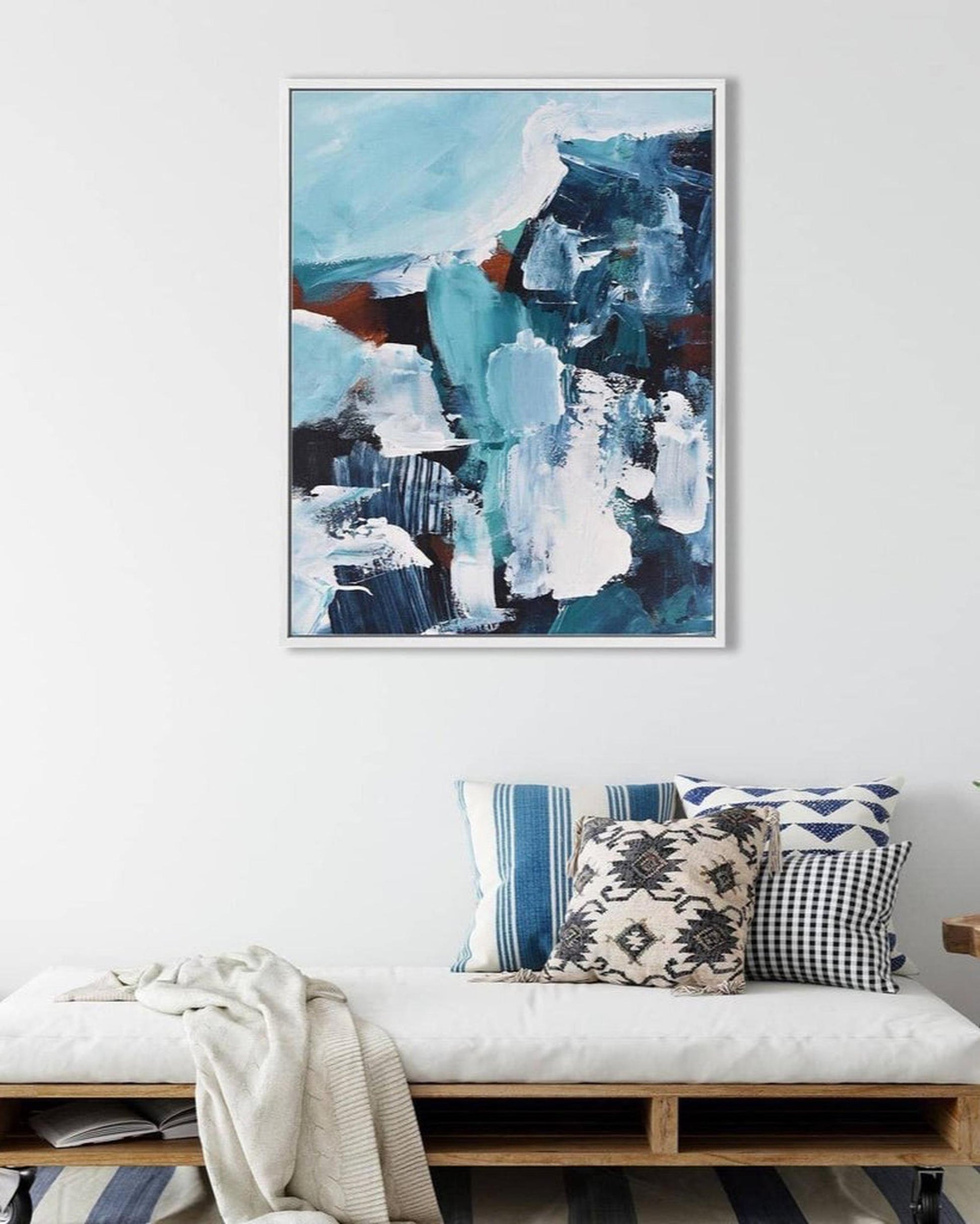 Abstract art painting on a wall above a bench with decorative pillows.
