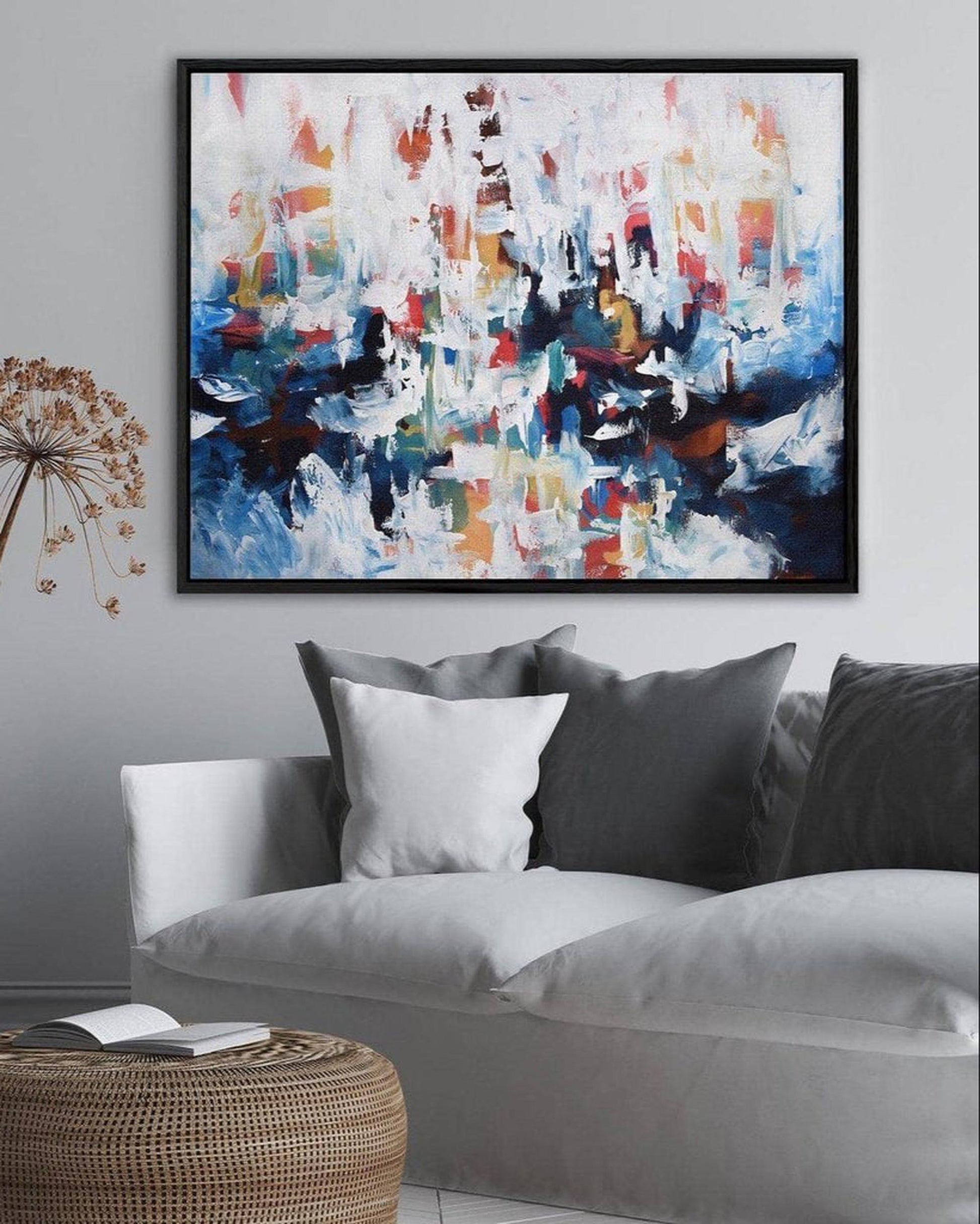 Living room with a gray sofa, wicker ottoman, and abstract painting on the wall.