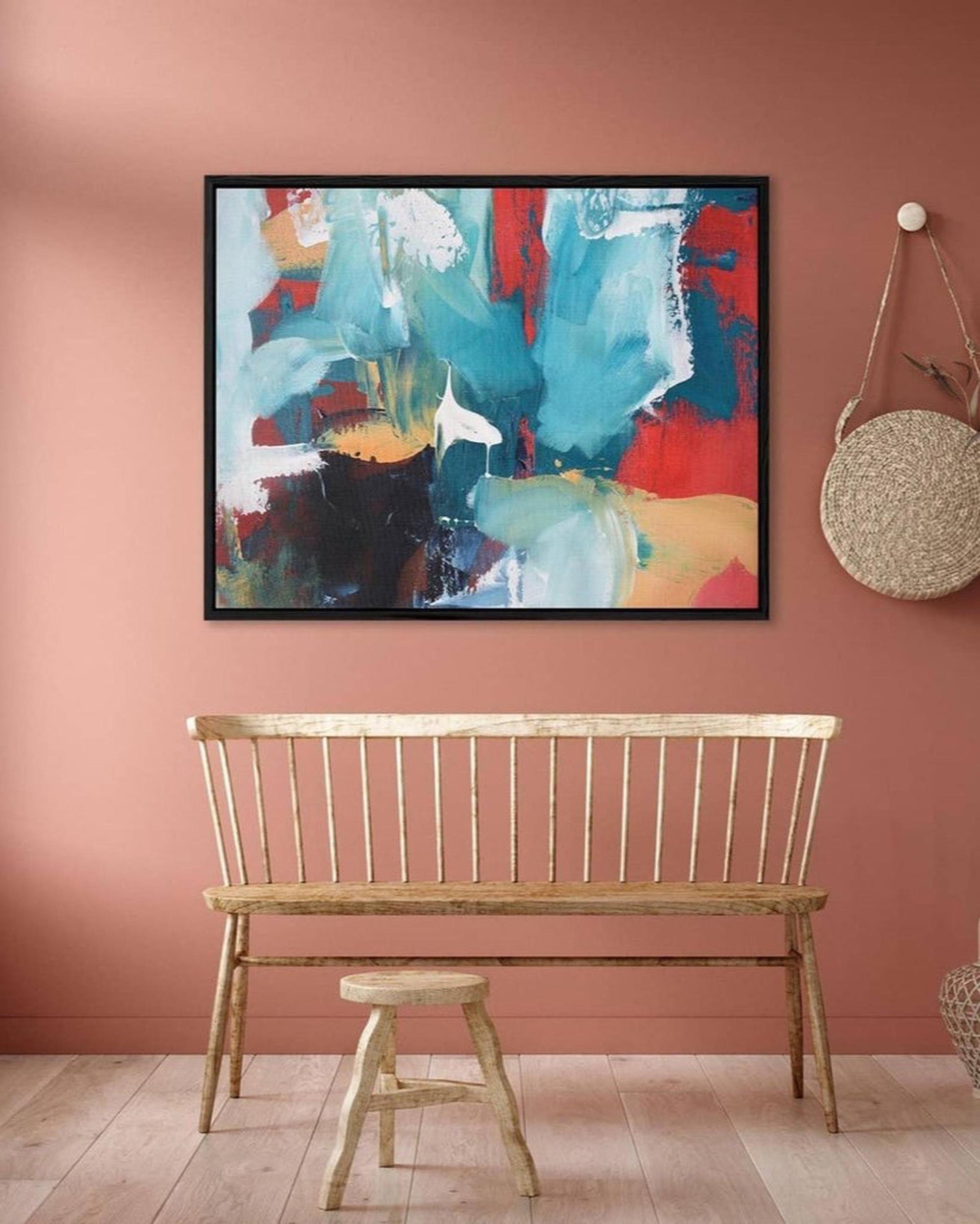 Abstract painting on a pink wall with a wooden bench below.