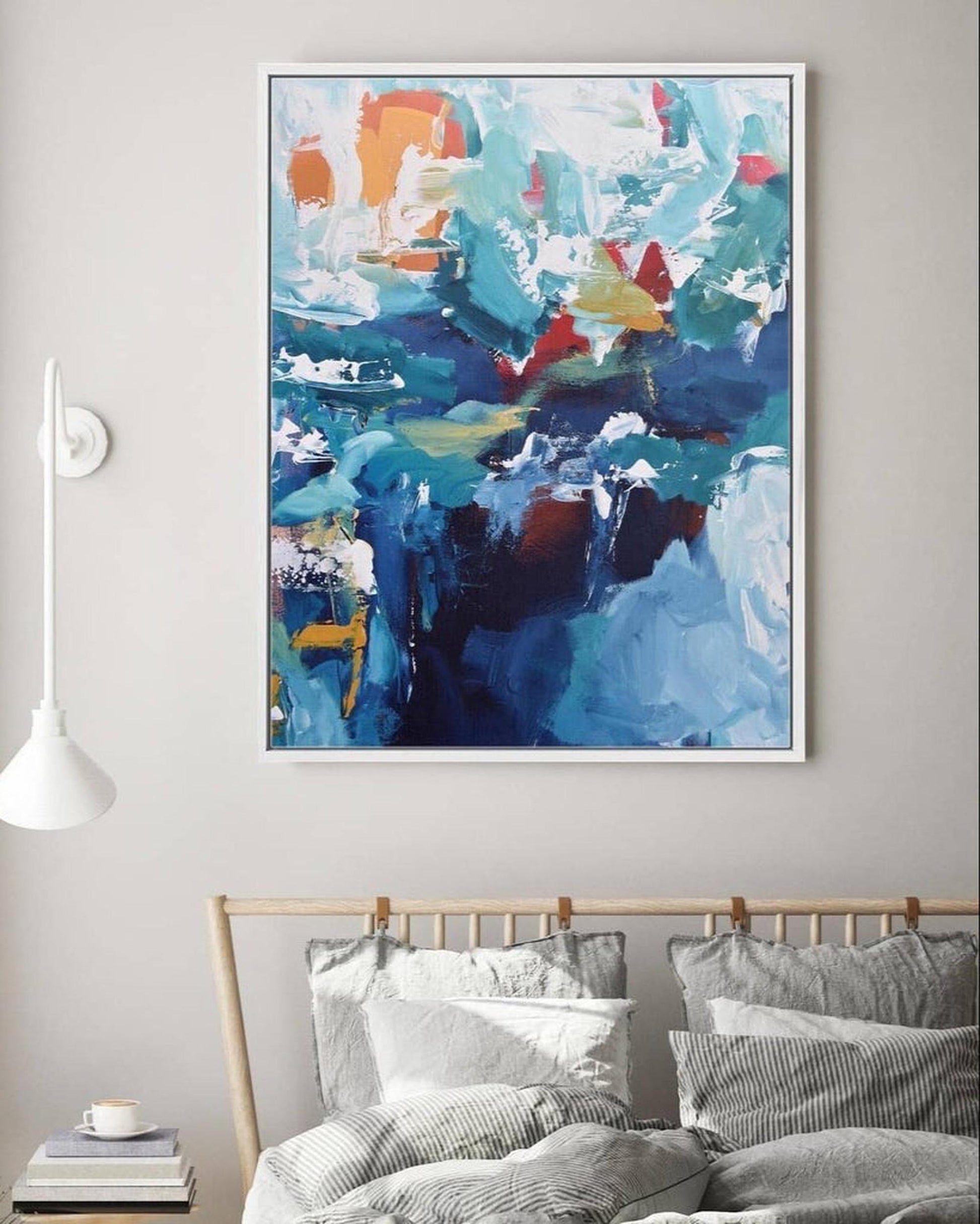 Abstract painting with blue, orange, and yellow colors on a gray wall above a bed.
