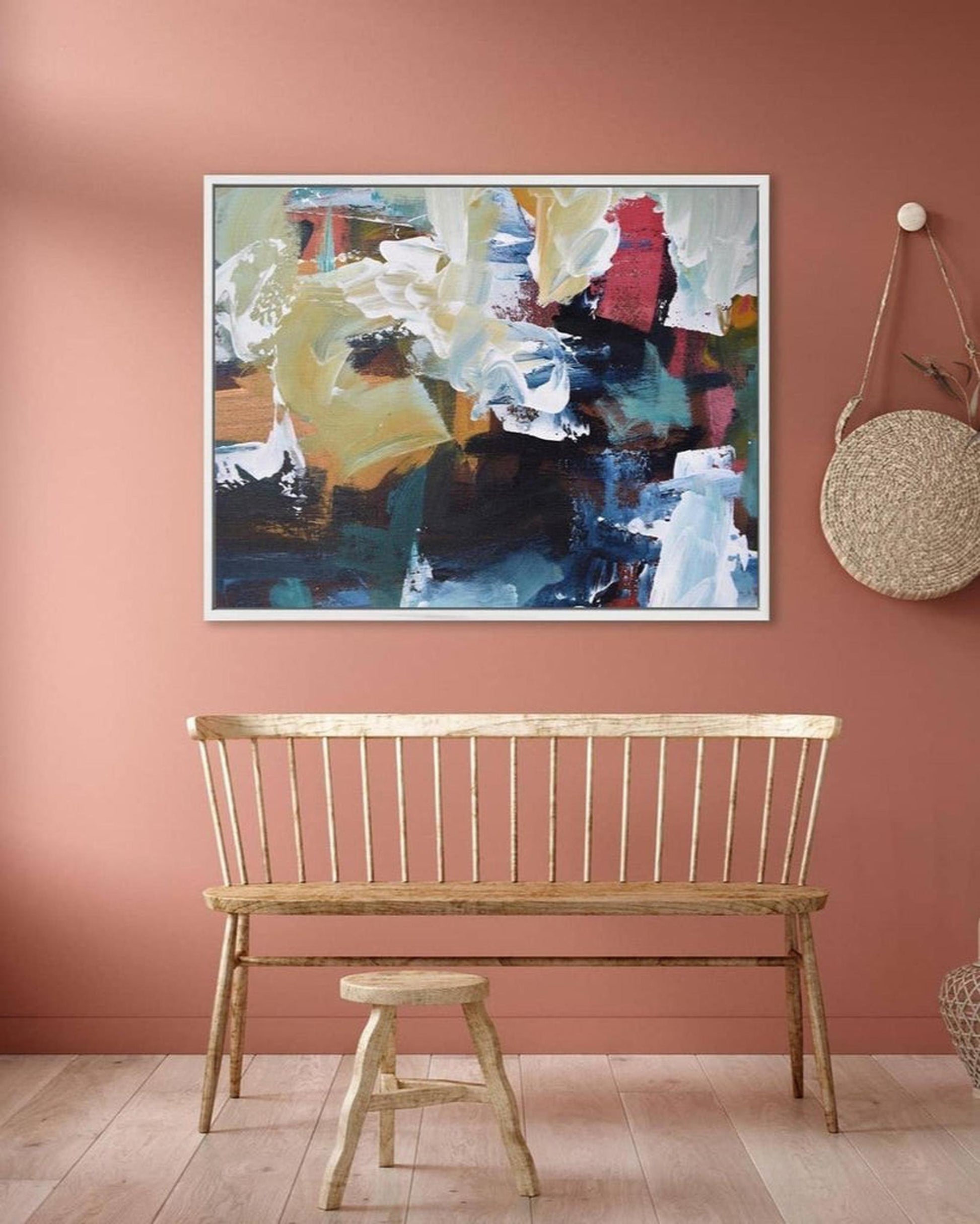 Wooden bench and stool in front of a colorful abstract painting on a pink wall.