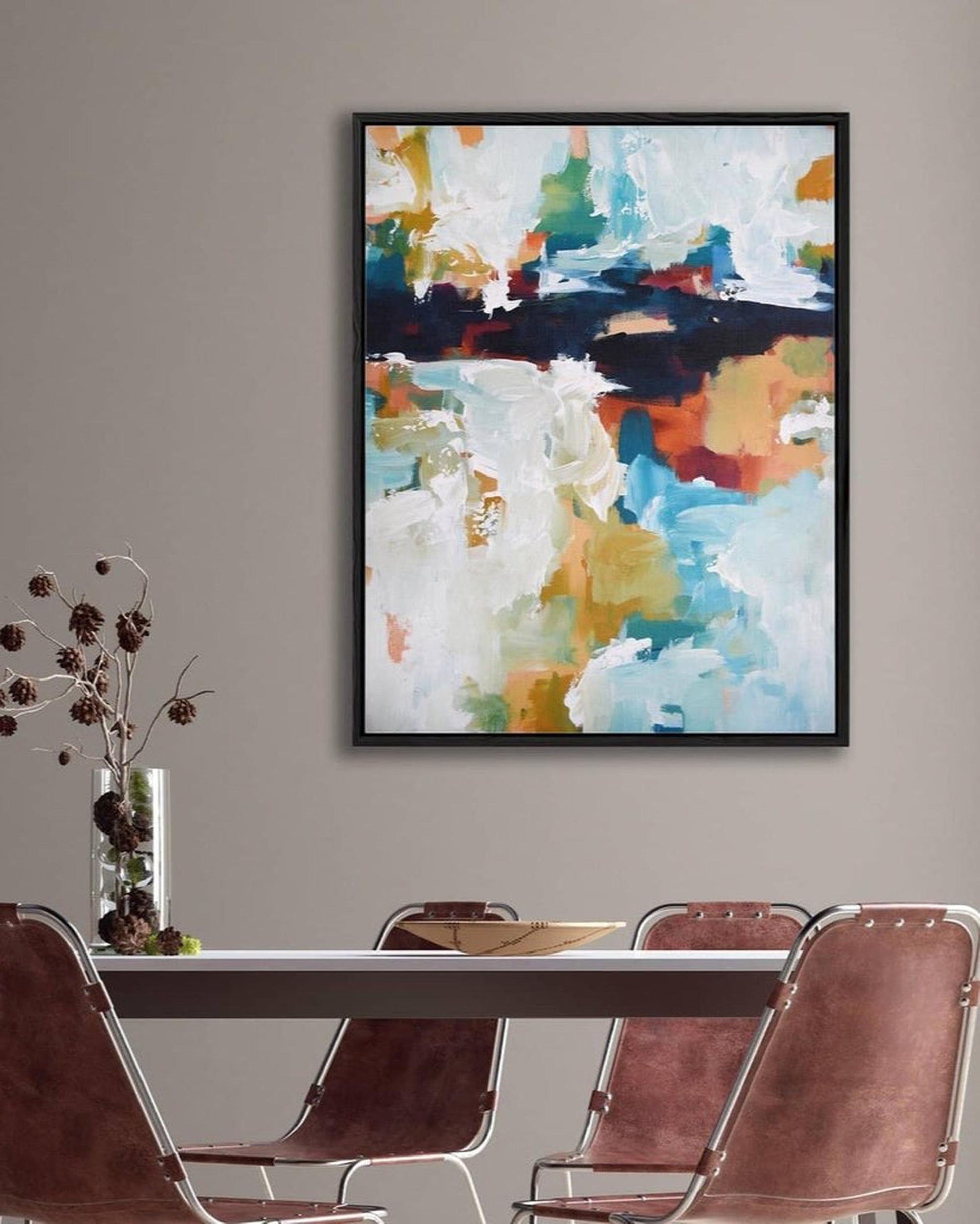 Abstract art piece on a wall above a dining table with chairs.