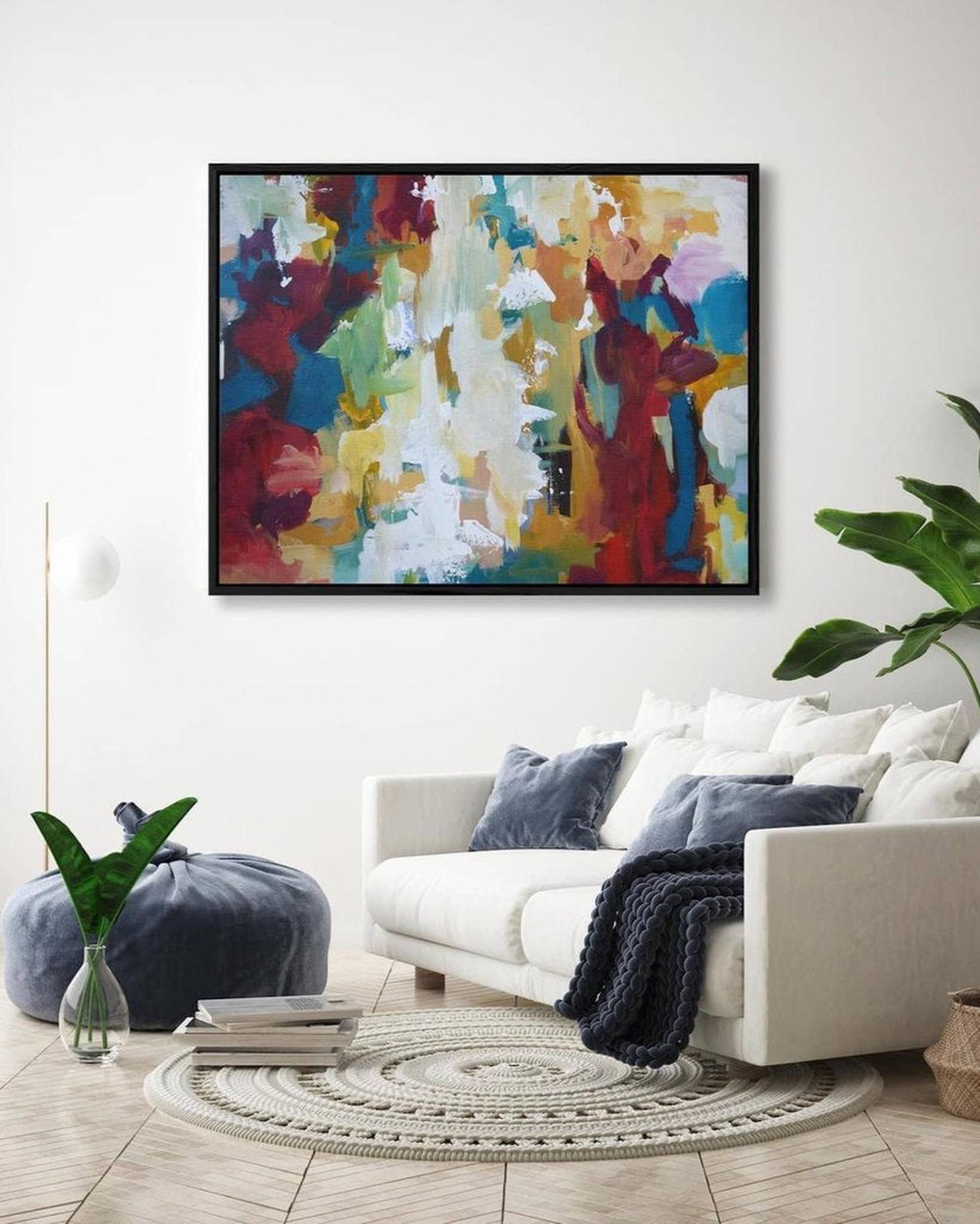 Colorful abstract painting on a wall above a white sofa with decorative pillows and a plant.