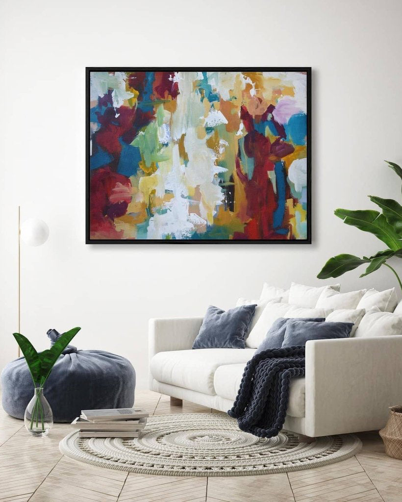 Colorful abstract painting on a wall above a white sofa with decorative pillows and a plant.