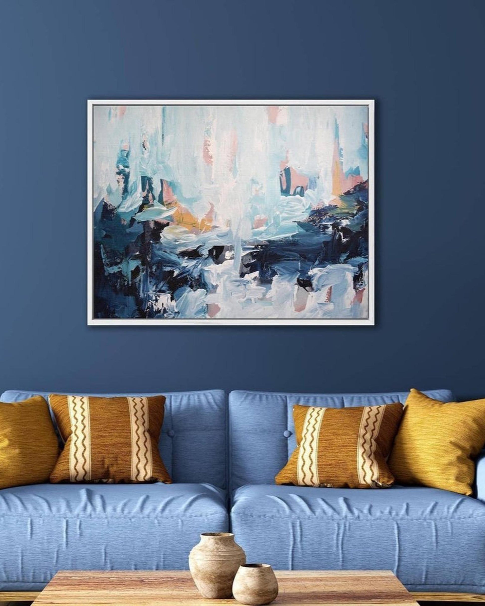 Abstract painting on a blue wall above a blue sofa with yellow pillows.
