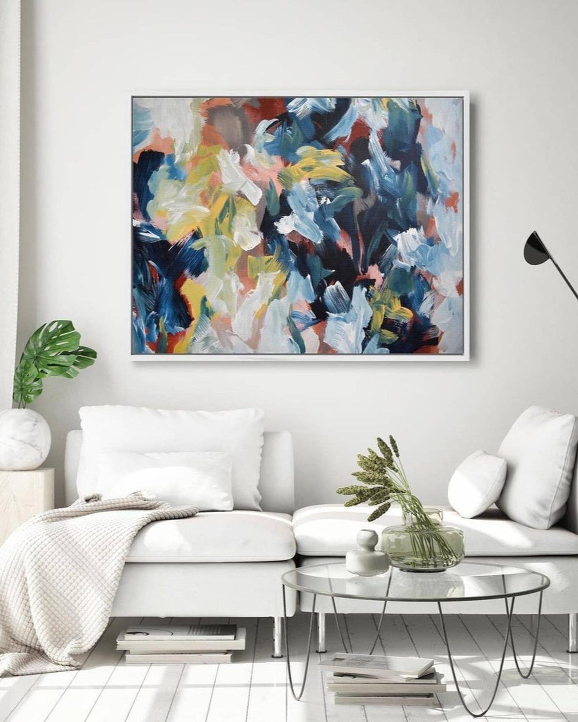 Abstract painting in a modern living room with a white sofa and glass coffee table.