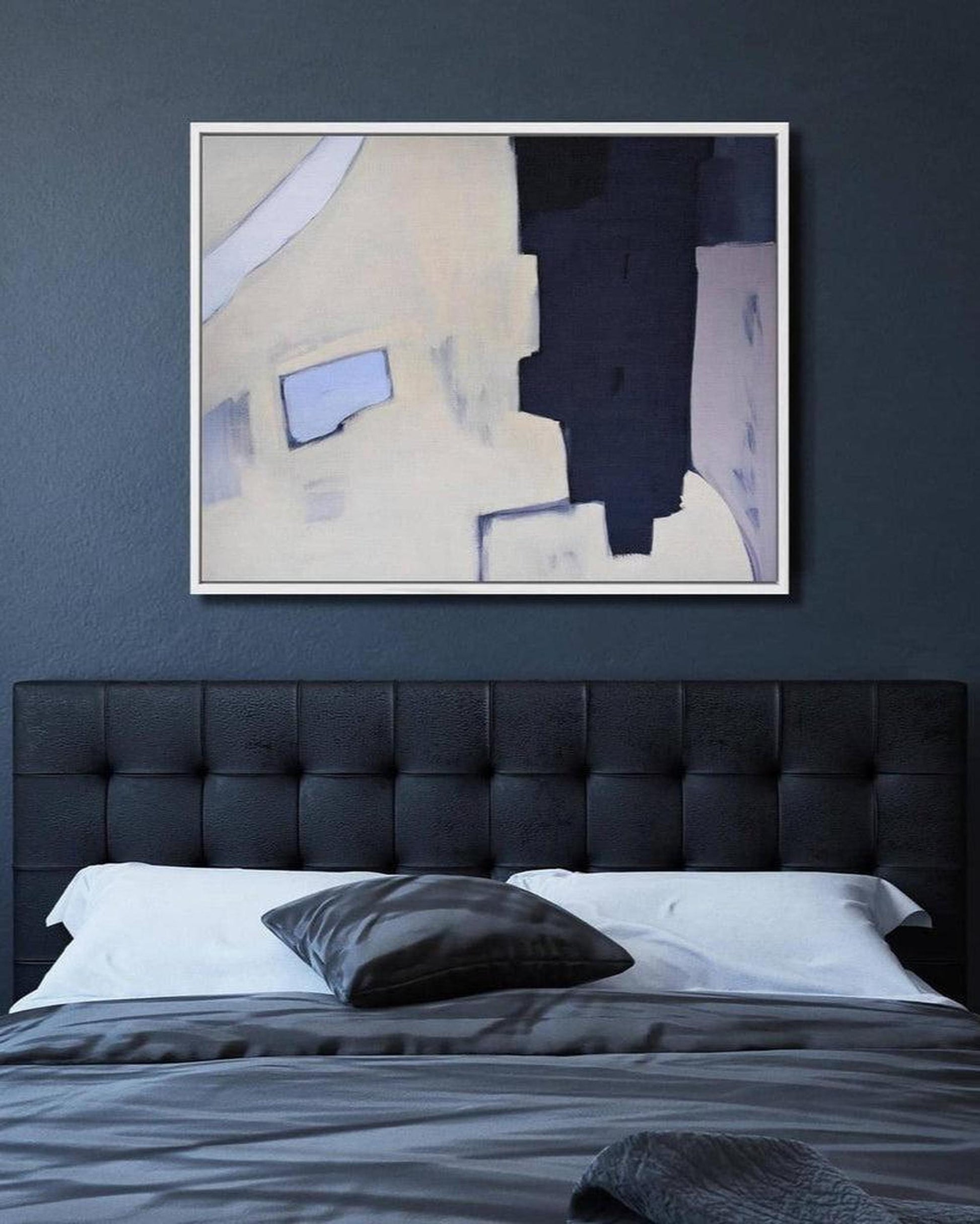 Abstract painting on a dark blue wall above a bed with a black headboard.