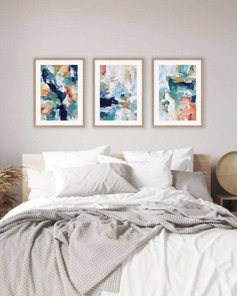 Three abstract art prints above a bed in a bedroom setting.