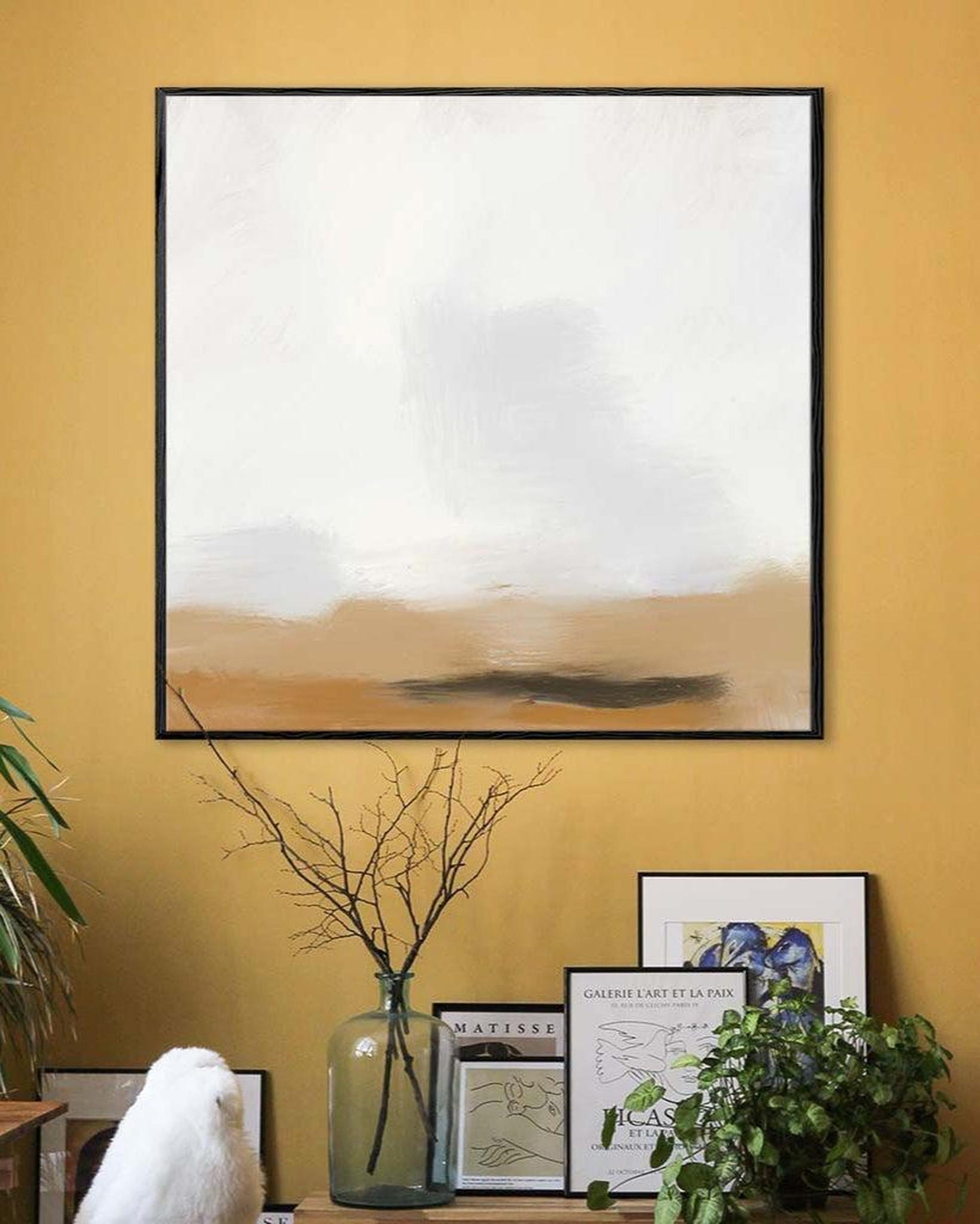 Framed abstract art on a mustard yellow wall with decorative elements.