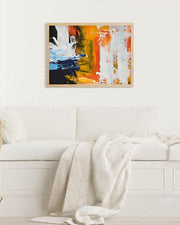 Framed abstract artwork featuring orange and yellow hues, displayed above a white sofa, with a wooden frame.