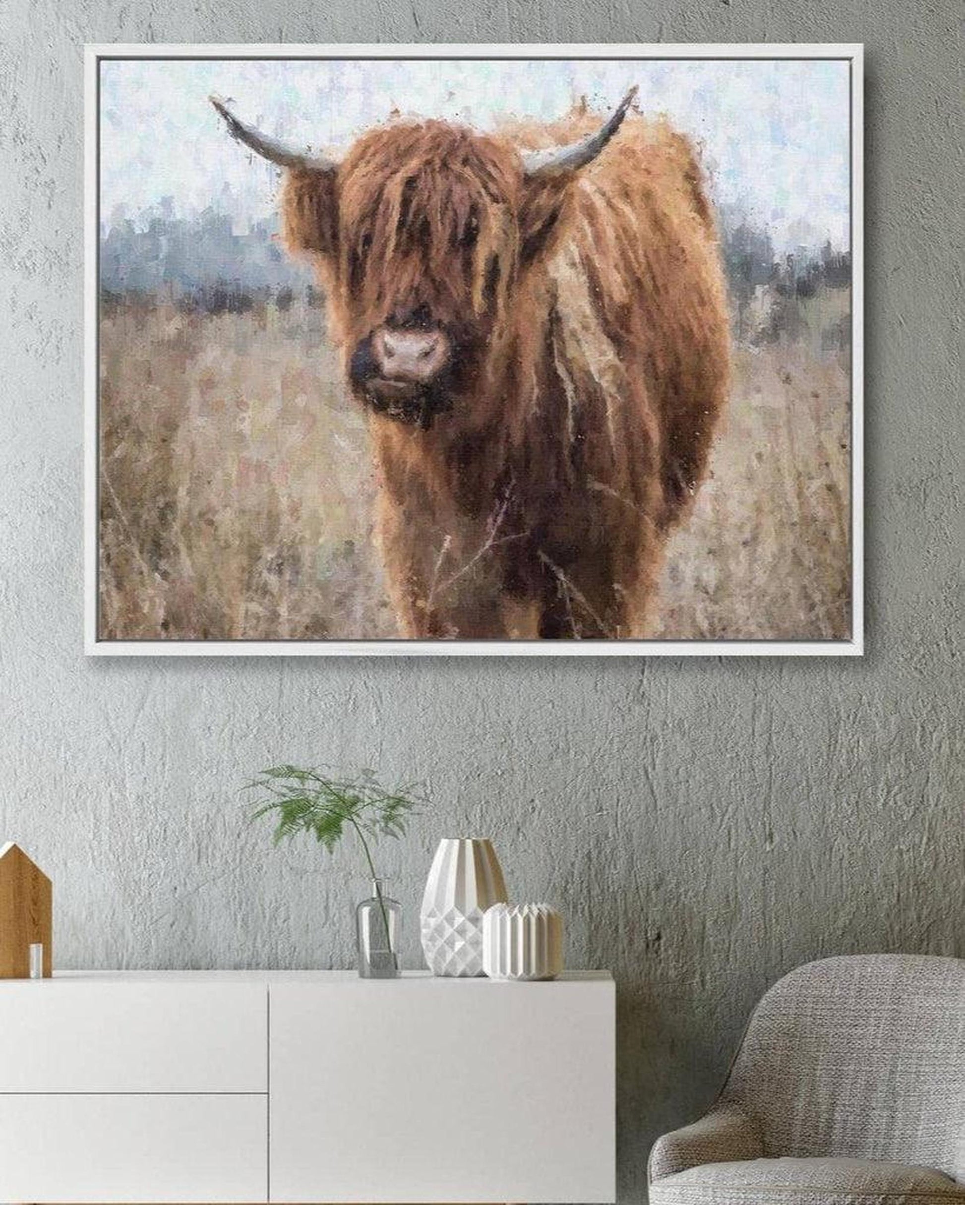 Framed artwork of a Highland cow in a field on a wall above a white cabinet.