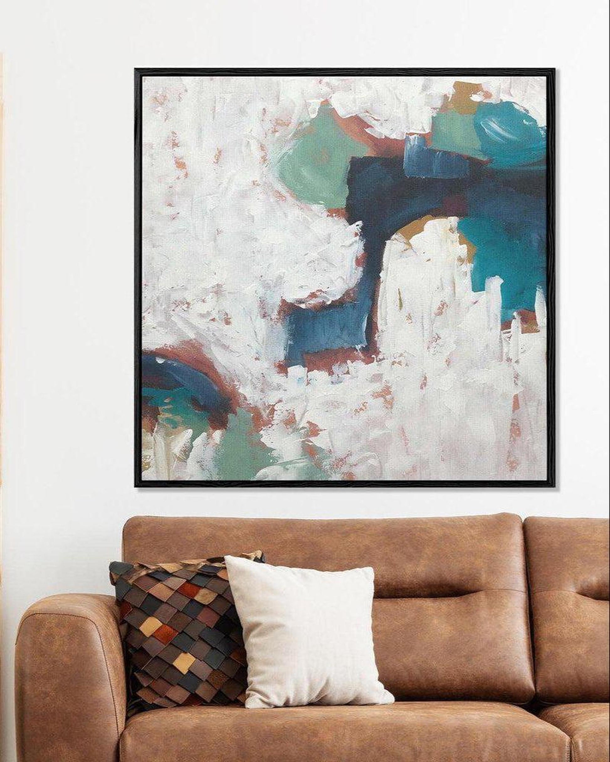 Abstract art piece on a wall above a brown sofa with cushions.