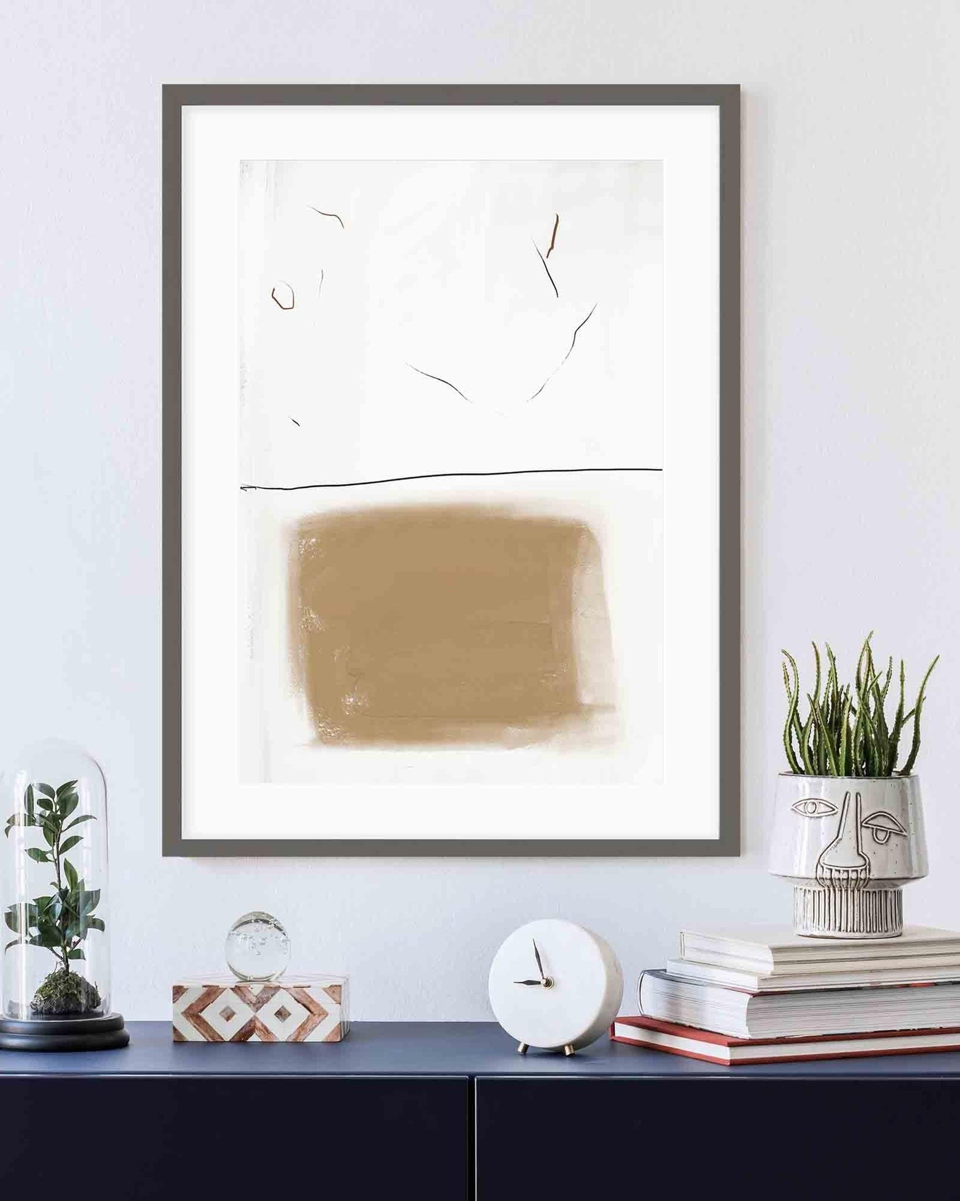 Framed abstract art piece on a wall with decorative items below.