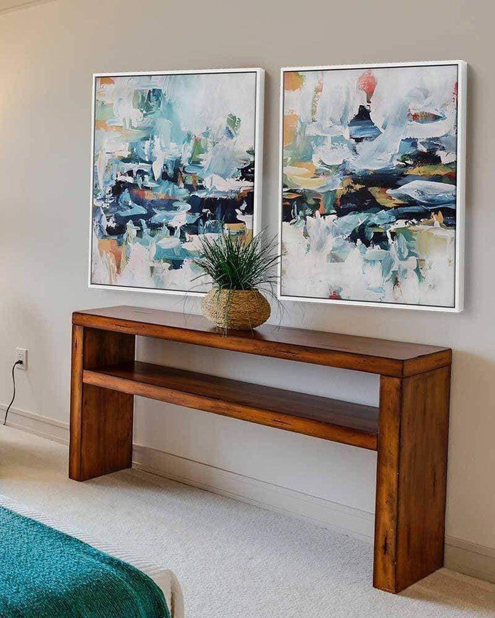 Two abstract paintings on a wall above a wooden console table in a room.