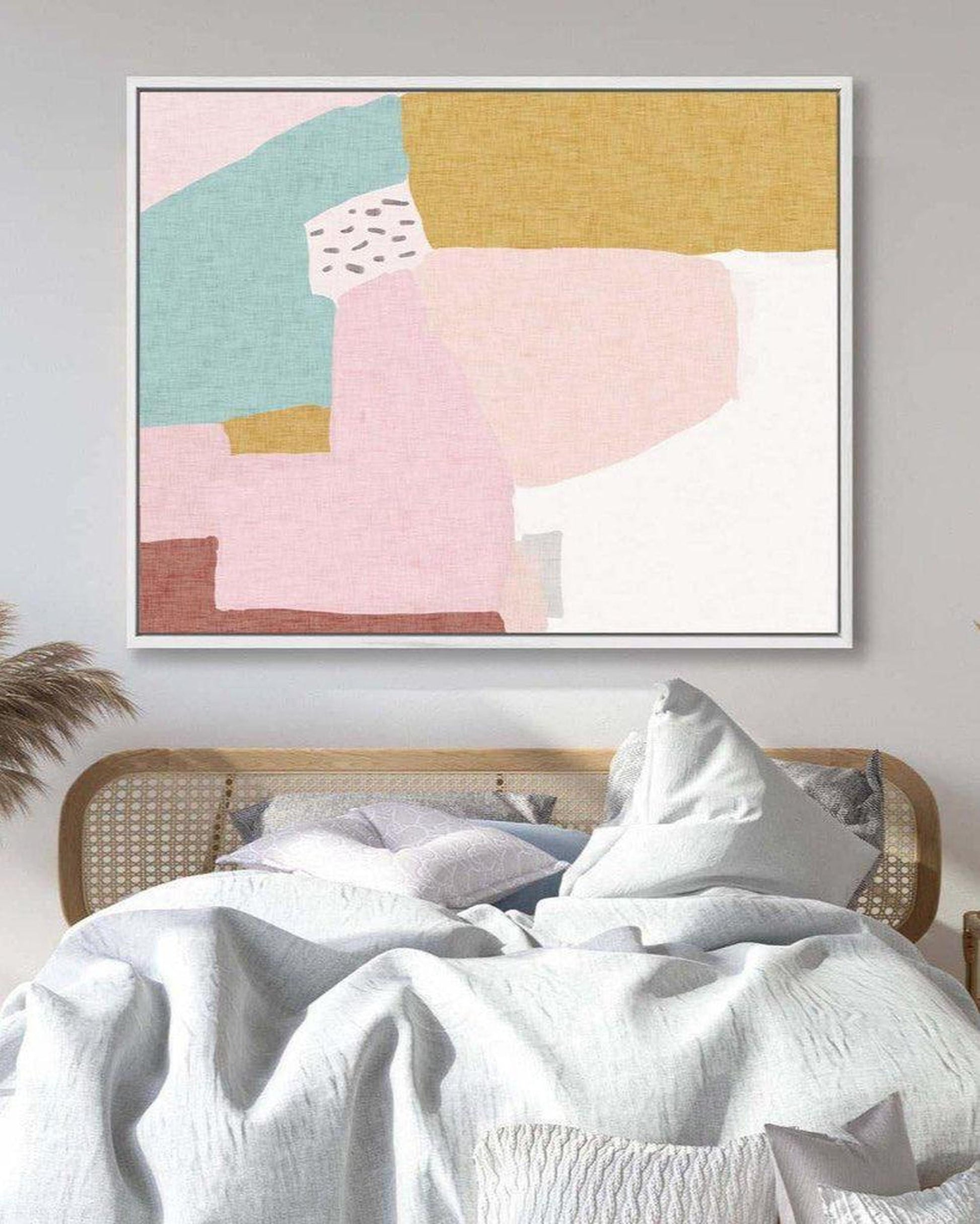 Abstract art print on a wall above a bed with white bedding and a wicker headboard.